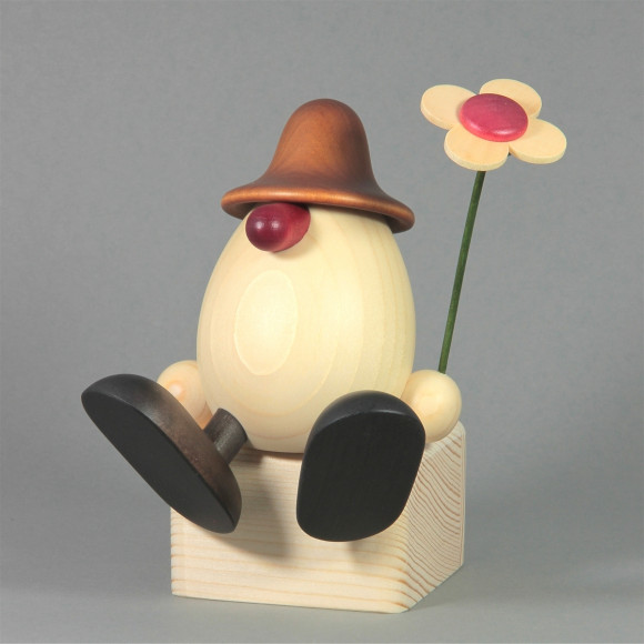 Eierkopf Anton mit Blume auf Kante sitzend, braun