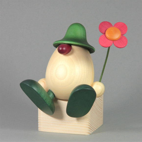 Eierkopf Anton mit Blume auf Kante sitzend, grün