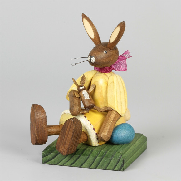 Kleines Hasenmädchen mit Puppe, sitzend, gelb