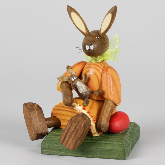 Kleines Hasenmädchen mit Puppe, sitzend, orange